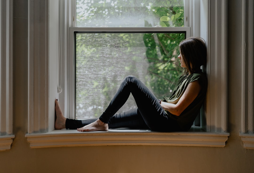 Person sitting alone on a window sill in soft light, in a quiet moment of recognition about a job that looks great but feels wrong.