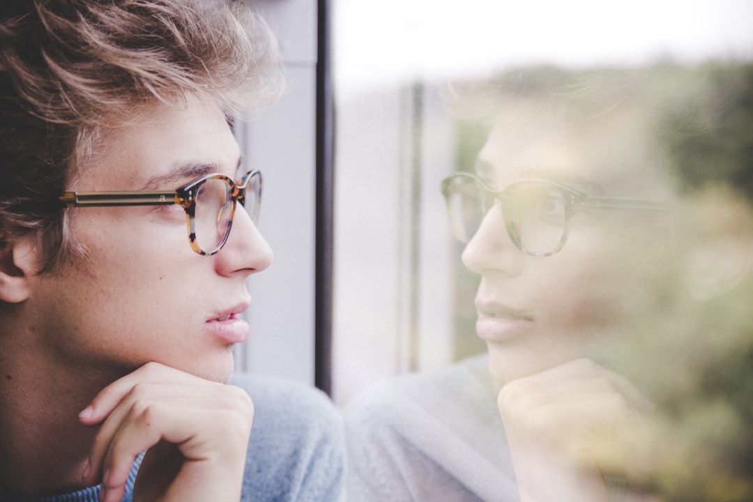 A man in glasses pauses to look out a window, weighing a decision before he commits - the careful mindset you need to evaluate company culture before accepting a job offer.