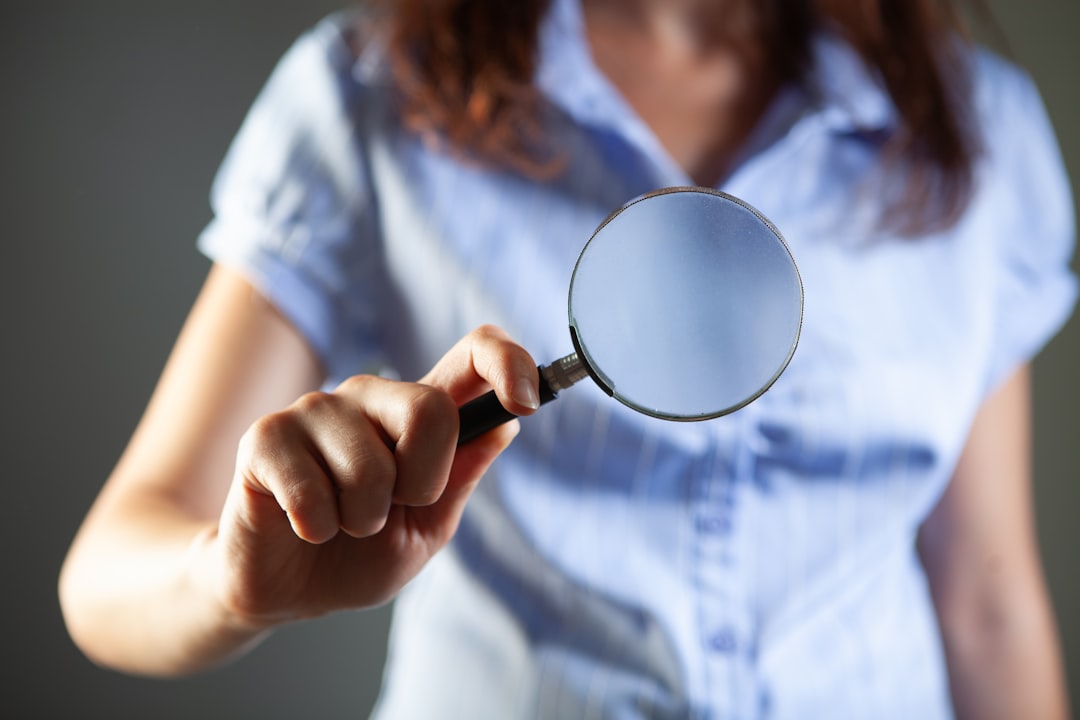 Person holding a magnifying glass toward the viewer, representing precise searching to find hidden job listings.