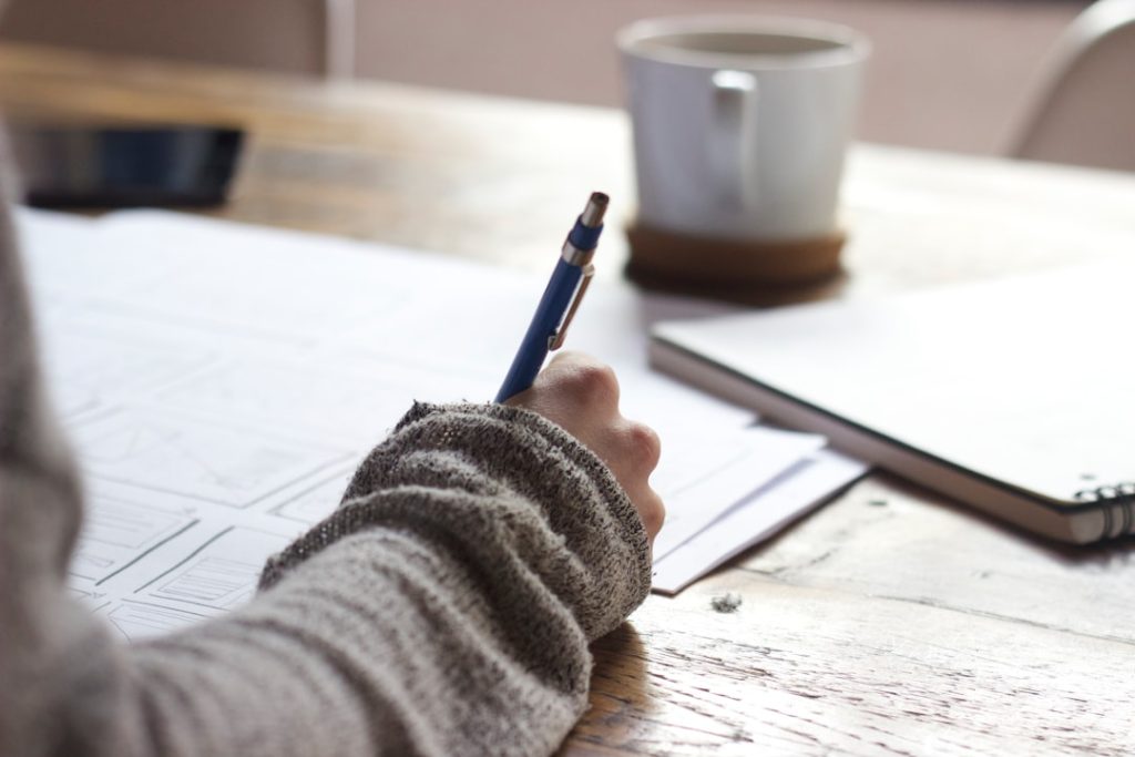 Job seeker at a wooden table writing a brief to prepare their job references before a reference check.