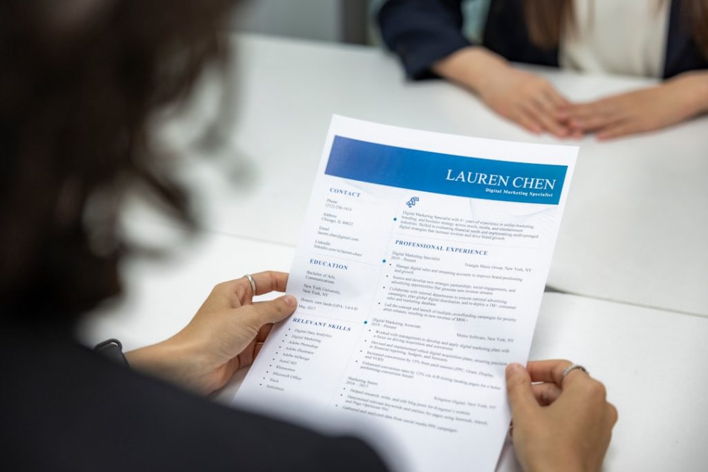 A job seeker at a table carefully reviewing a printed resume before it goes into an applicant tracking system.