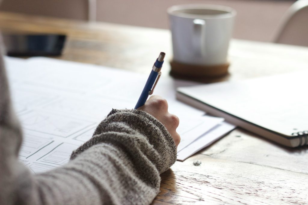 A person sketching plans and notes by hand at a wooden table - the deliberate, focused strategy a tech job search takes.