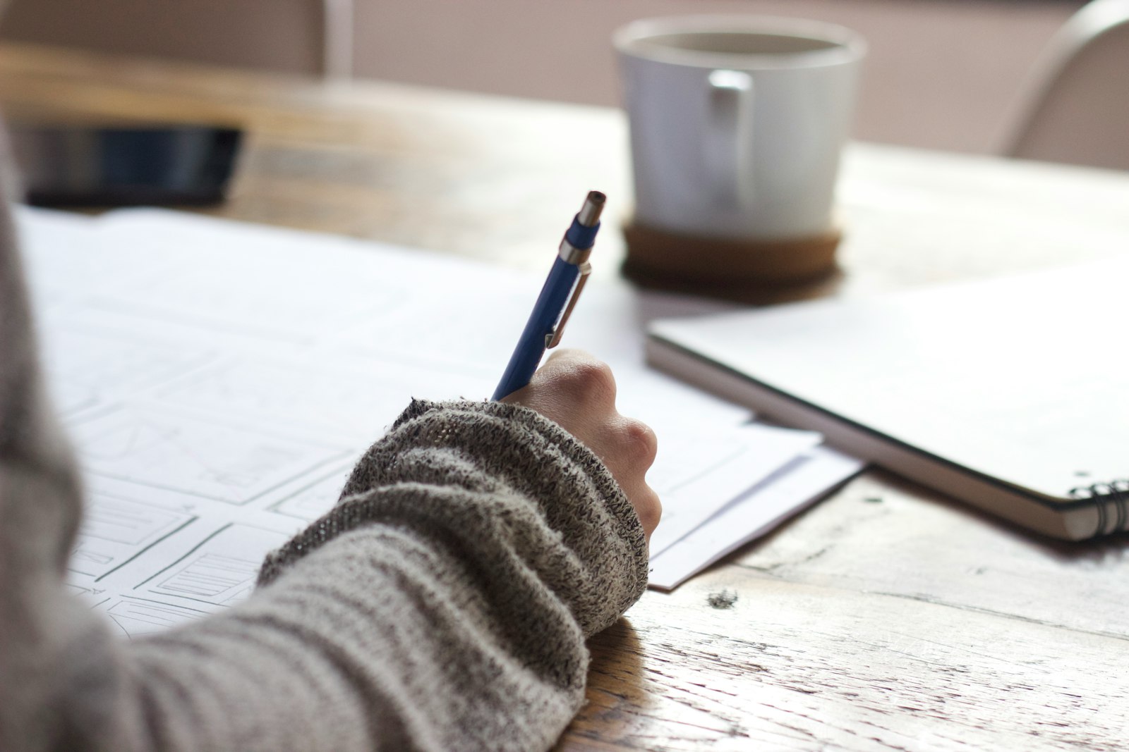 A person sketching plans and notes by hand at a wooden table - the deliberate, focused strategy a tech job search takes.