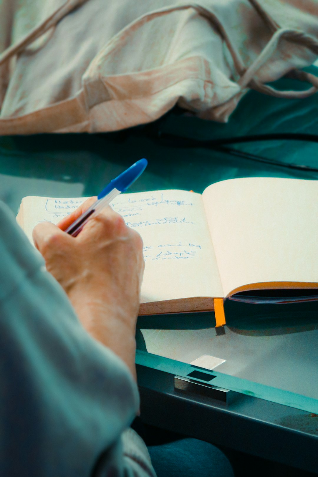 A person sitting at a table taking notes in a notebook, the way a candidate should capture intel during a recruiter phone screen