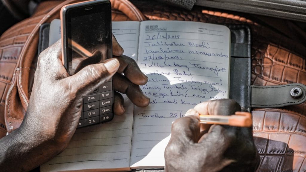 A person taking handwritten notes on a notepad while holding a phone during a call, preparing their salary expectations before answering.