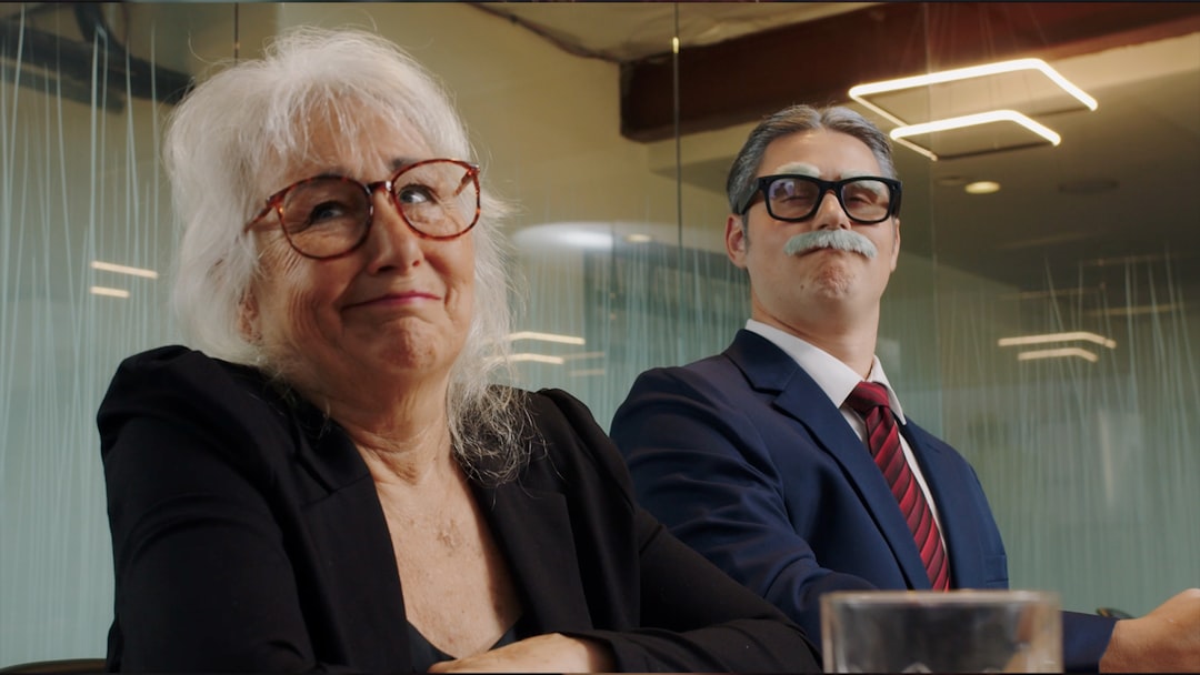 Two experienced professionals with grey hair sitting confidently together in a modern glass-walled office conference room