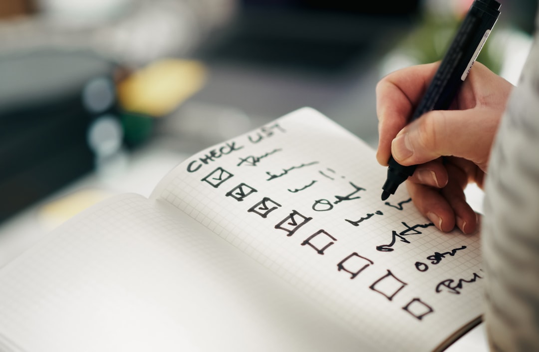 A hand holding a marker ticks off the first four boxes on a handwritten page headed CHECK LIST in a grid notebook.