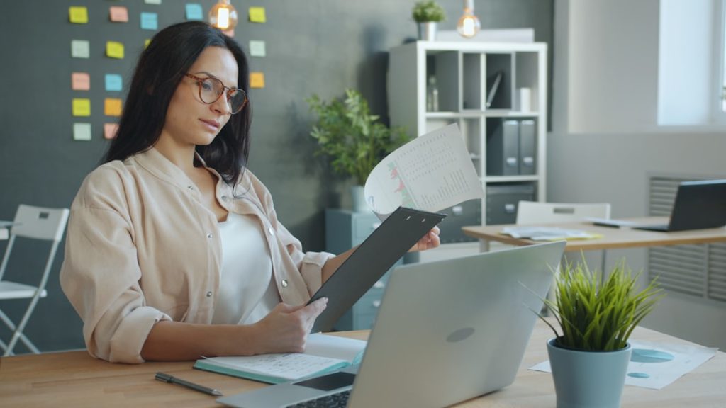 A professional at an office desk reviewing a document of charts and figures, checking the numbers before a compensation conversation.