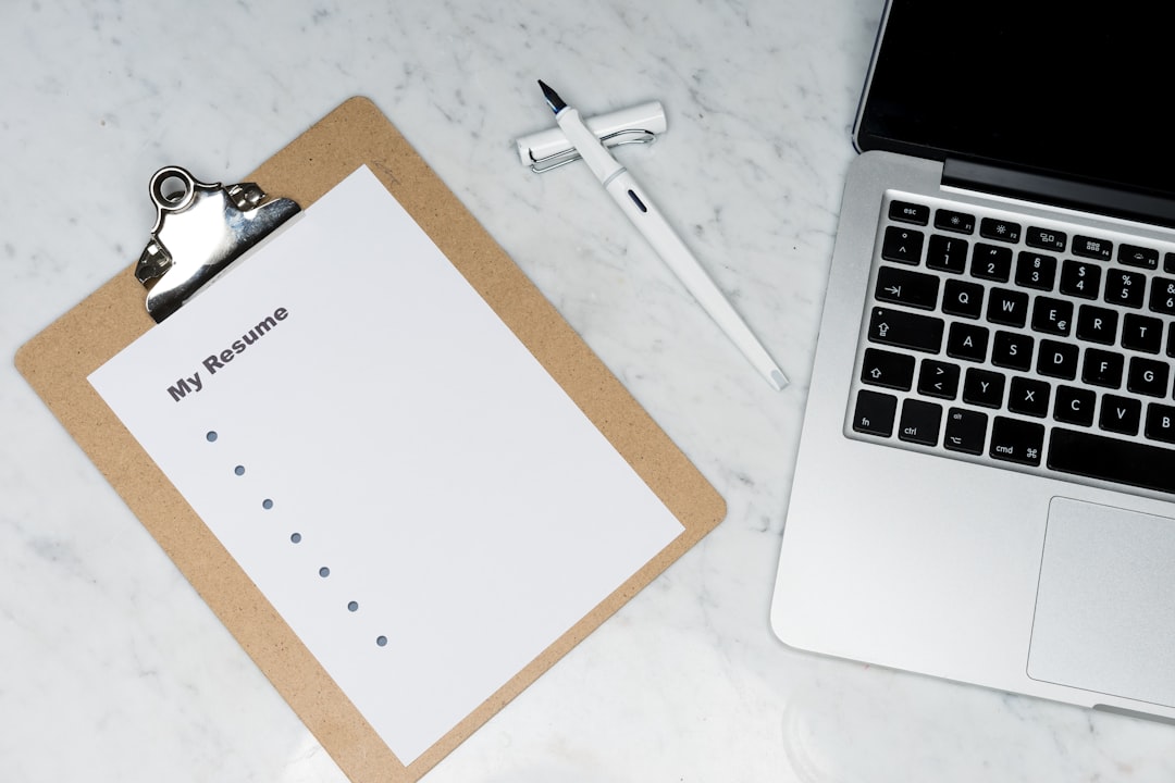 A clipboard on a marble desk holding a sheet titled My Resume with a column of empty bullet points, beside a white pen and an open laptop.