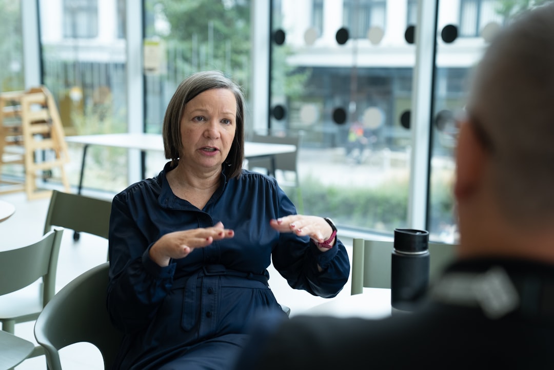 A woman in a navy shirt gestures with both hands as she speaks to a person seated across a small table, mid-answer in a one-on-one interview conversation.