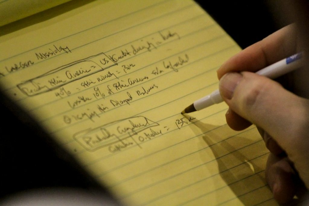 Close-up of a hand writing notes and figures on a yellow legal pad, with results boxed and a dollar total at the bottom