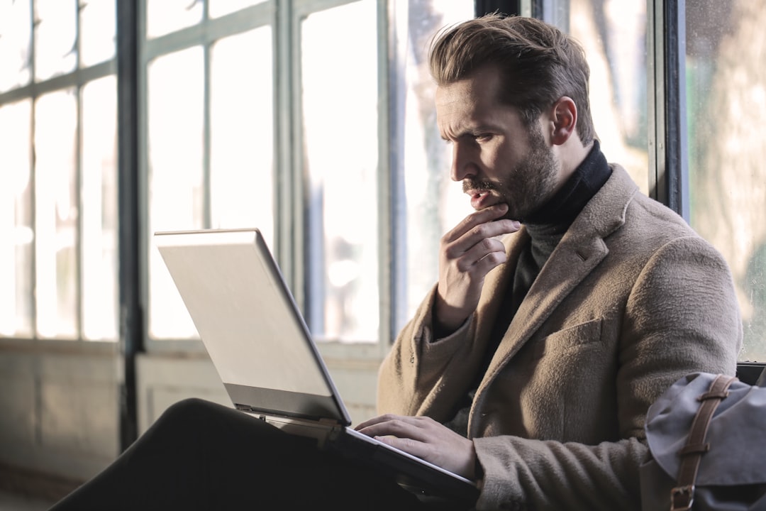 A man in a camel coat frowns at his laptop screen with his hand on his chin, working out what a final interview rejection email actually means