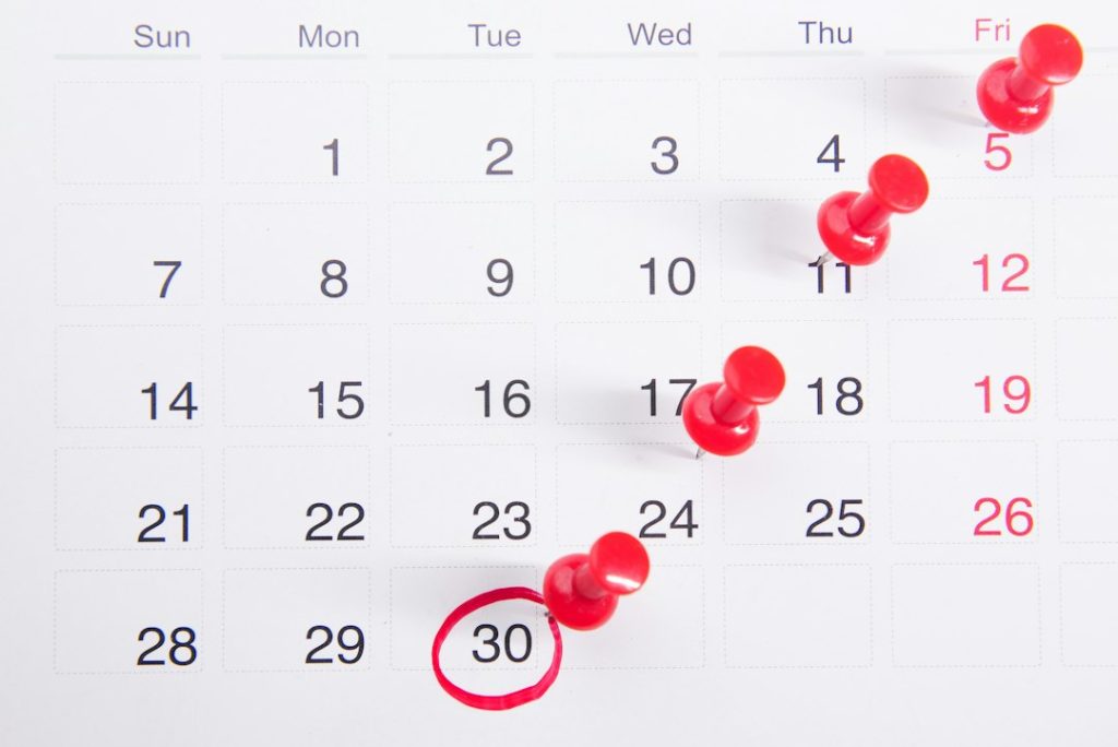 Paper calendar with red push pins marking one date each week, stepping down to a final date circled in red