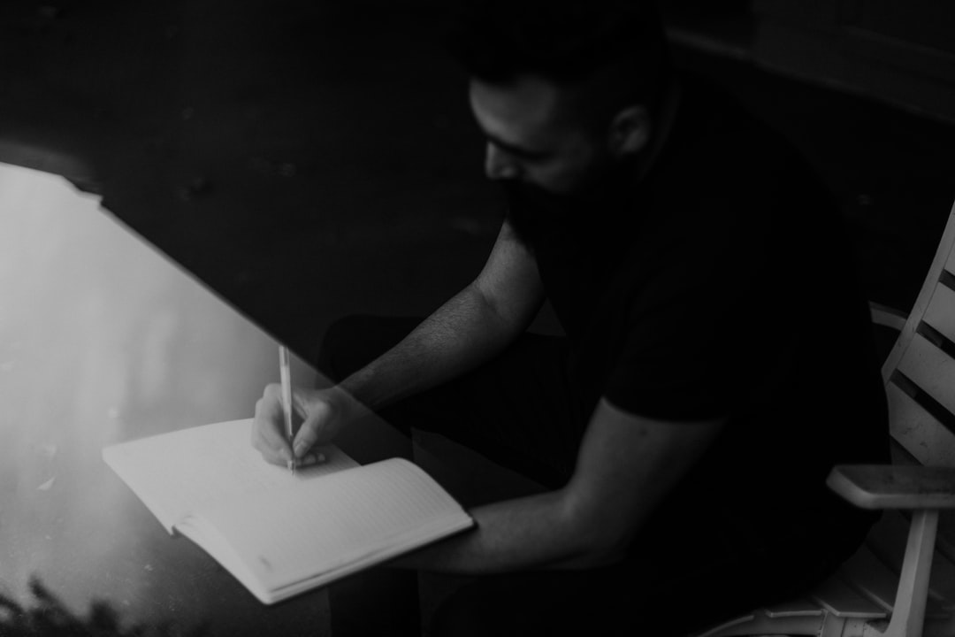 A person sitting alone at a table, writing by hand in an open lined notebook.