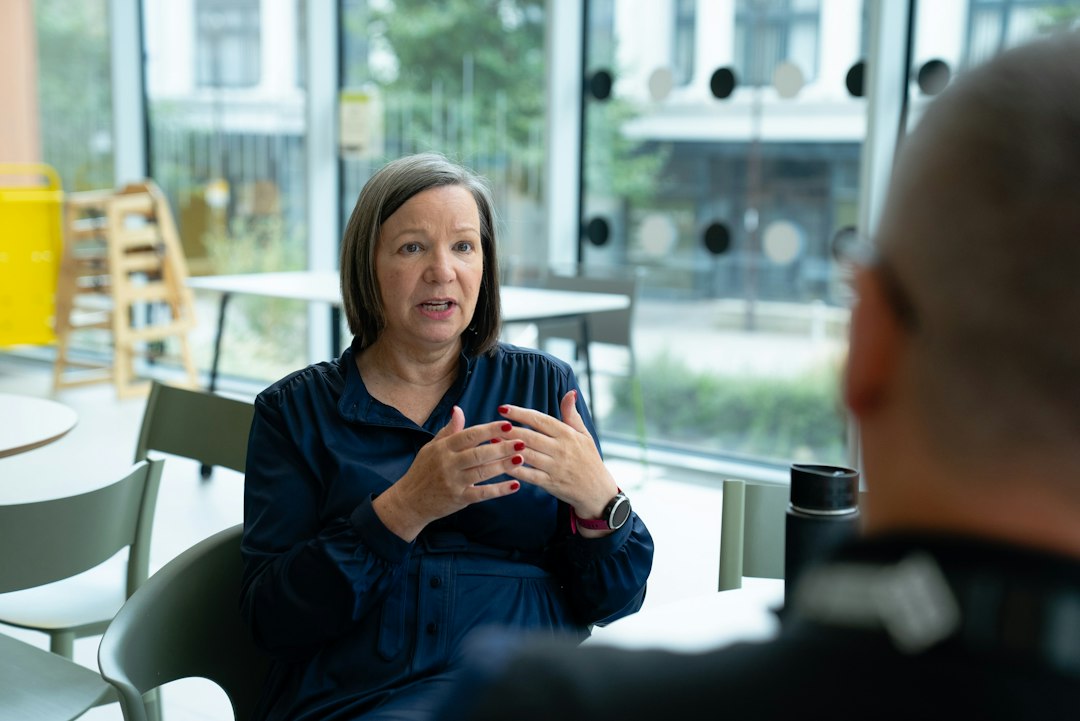 Experienced professional woman with gray-streaked hair explaining her point with both hands to a person across a cafe table