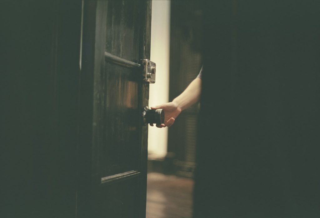 A hand pulling open a dark wooden door into a warmly lit room, the person going back in through a different door.