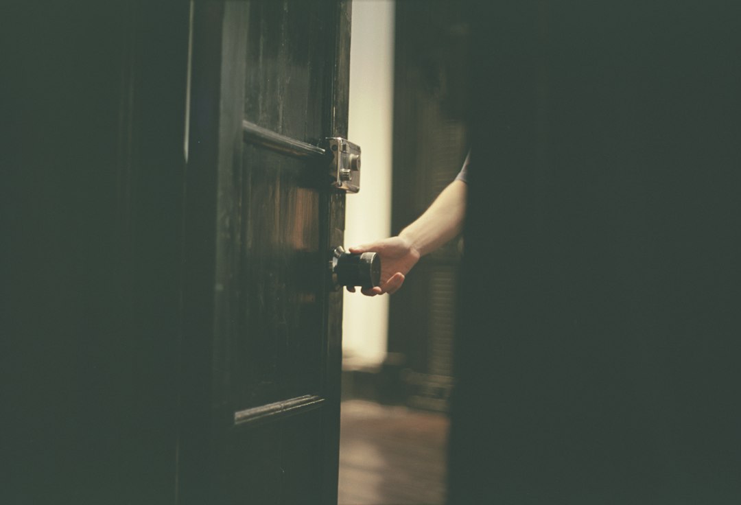 A hand pulling open a dark wooden door into a warmly lit room, the person going back in through a different door.