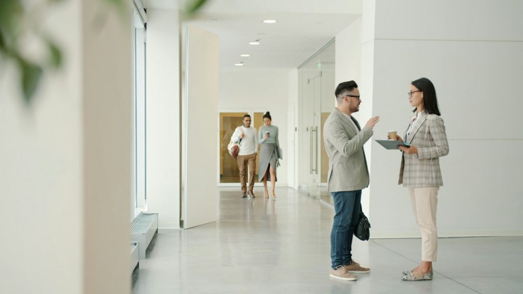 Two professionals in conversation in a bright modern office hallway while two colleagues walk toward them