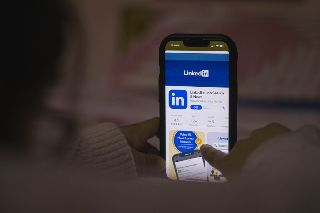 Hands holding a smartphone in a dim room, showing the LinkedIn Job Search and News app page