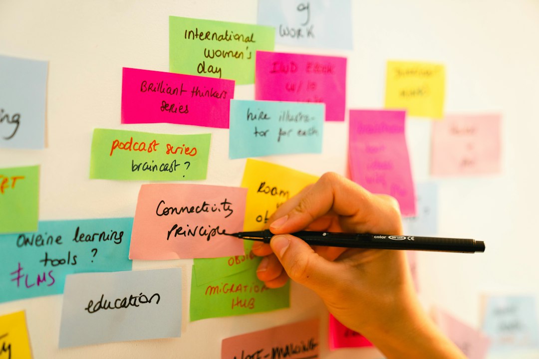 A hand writing on a pink sticky note on a wall covered with colorful handwritten notes, like a story being mapped out beat by beat