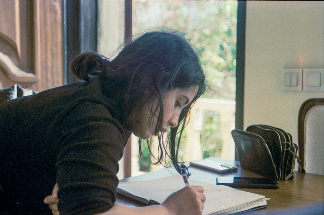 A person writing in a notebook at a wooden desk by a window, planning ahead